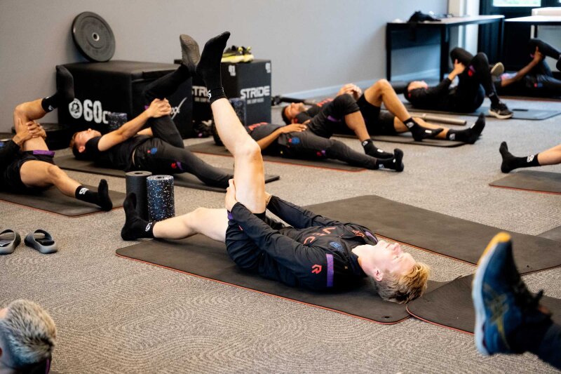 Spelers doen stretchoefeningen op matten in de fitnessruimte.