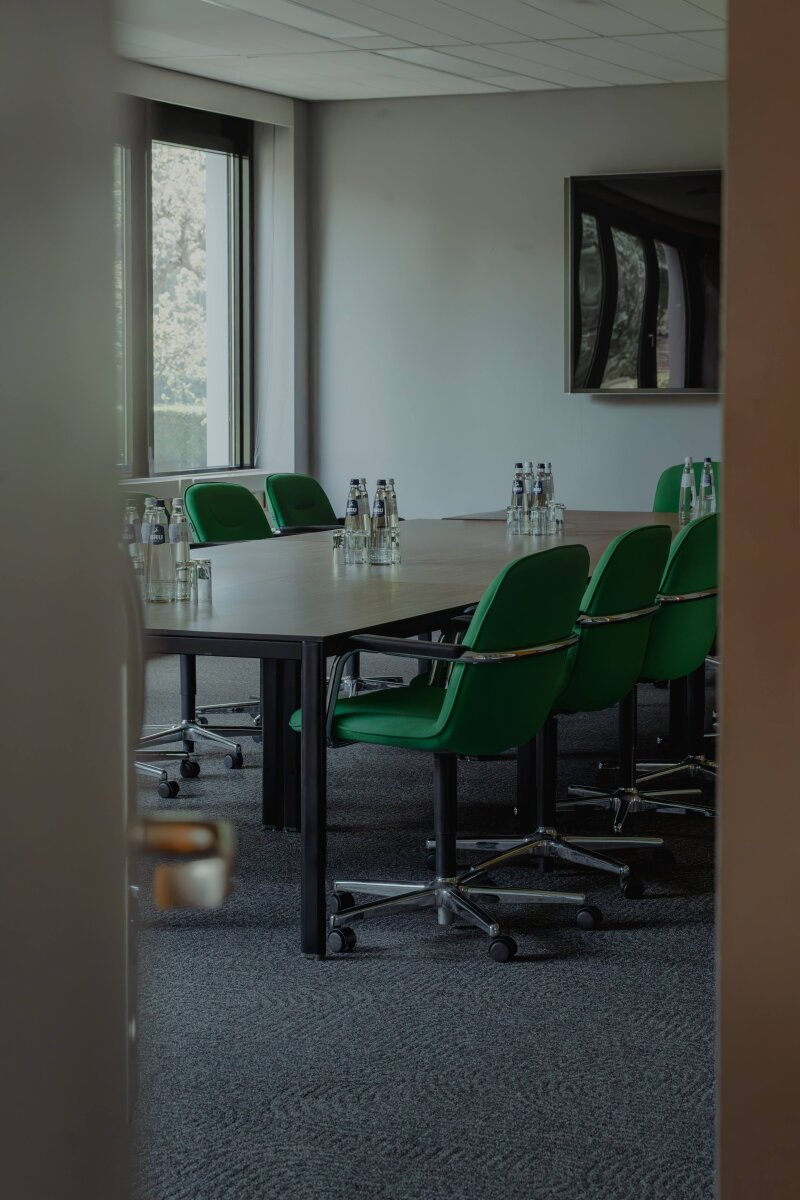 Vergaderzaal met groene stoelen en daglicht.