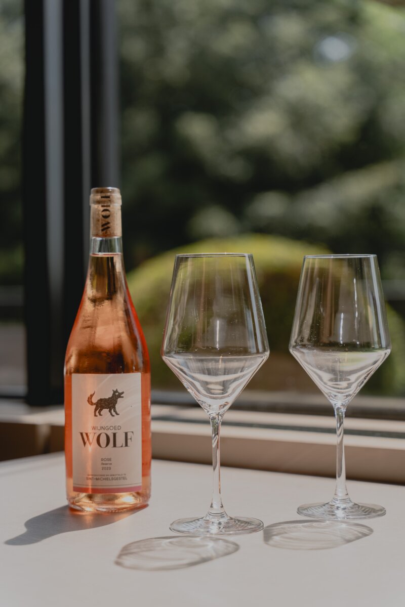 Fles rosé en twee glazen op tafel bij het raam.